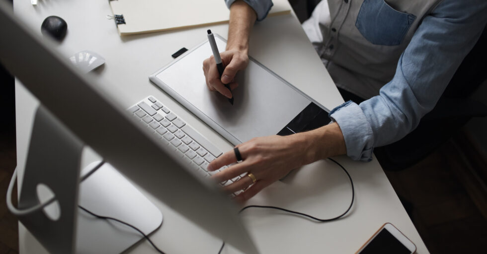 Designer hands using graphics tablet while working with computer at studio or office. Top side view.